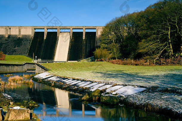 在寒冷的冬日（蓝天），Thruscross水库的高而陡的混凝土坝反射在河道中流动的水上——英国英格兰约克郡北部