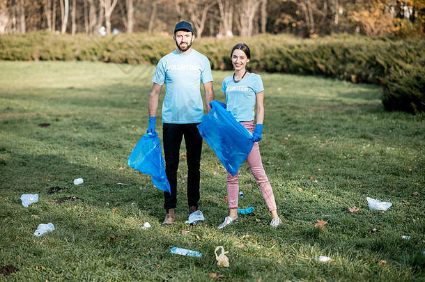 肖像男人。女人志愿者穿着蓝色的t恤清洁公共花园塑料垃圾袋