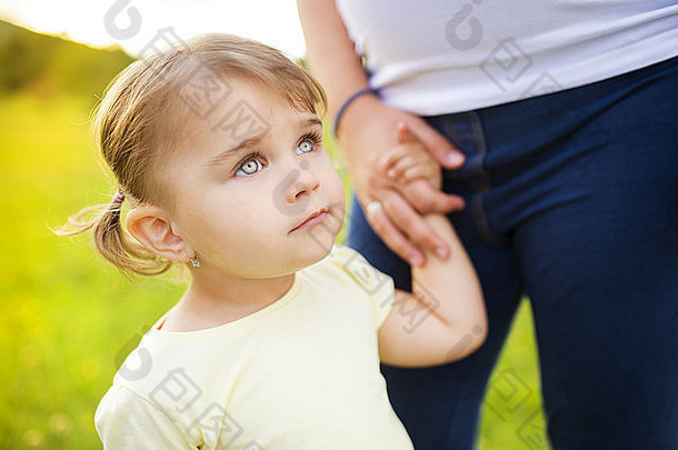 公园里快乐的小女儿牵着怀孕母亲的手的画像
