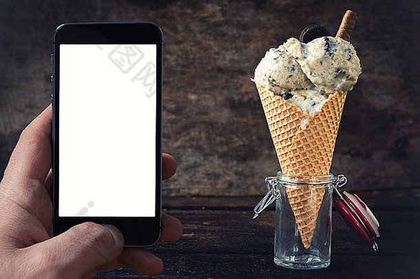 木质背景上有饼干的冰淇淋，手机屏幕上有空白