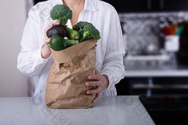 一名高加索妇女拿着装满绿色蔬菜的棕色袋子。