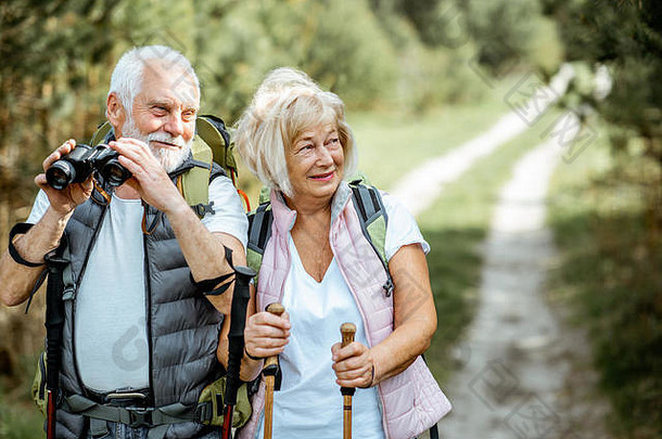 肖像快乐高级夫妇站双筒望远镜背包徒步旅行棒徒步旅行森林概念活跃的生活方式退休