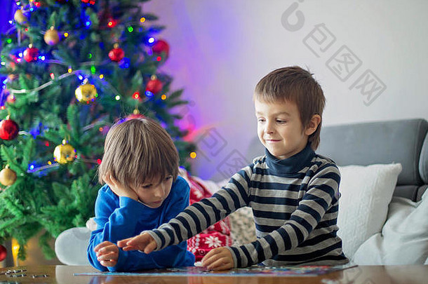 圣诞节，两个可爱的孩子坐在沙发上，在家里收集谜题，身后是圣诞装饰品