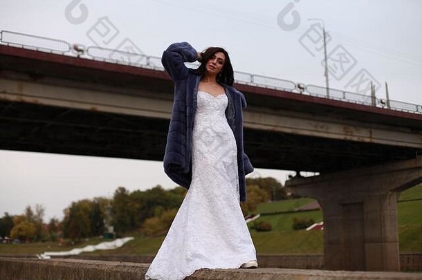 都市时尚<strong>婚纱摄影</strong>，新娘穿着紫色貂皮大衣外出，站在桥旁，低角度观看，广告理念。