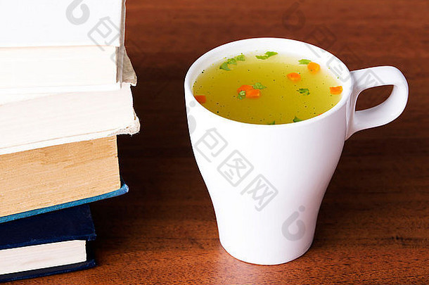 在书旁边的桌子上放一杯热蔬菜汤。