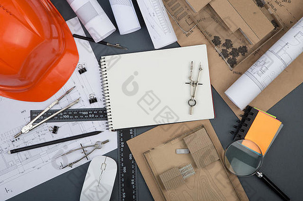 建筑师工作场所-空白便笺簿、施工图和工程工具、放大镜、灰色背景头盔