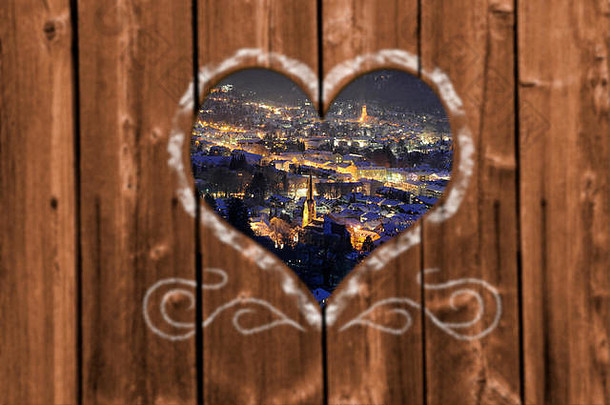 在寒冷的冬夜，透过木墙上雕刻的心形，眺望德国巴伐利亚的加米什·帕滕基琴市