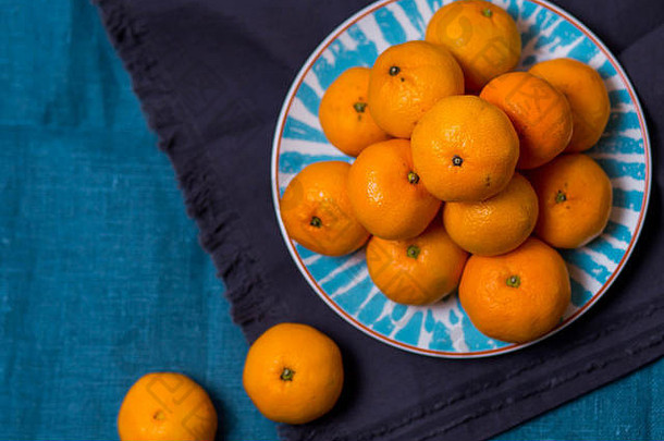 三个成熟美味多汁的柑桔躺在一个明亮的白色与蓝色的盘子图案的织物布厨房毛巾