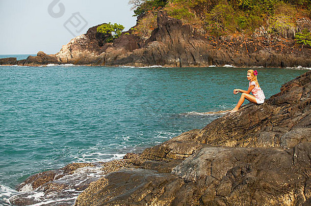 美丽的女孩坐在海边的岩石上