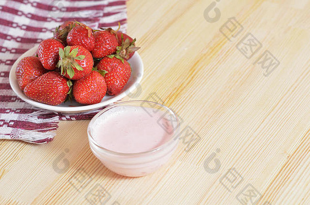 成熟的草莓放在<strong>碟</strong>子上，站在一张铺着桌布的木桌上，旁边是一个盛着奶<strong>油</strong>的<strong>碟</strong>子