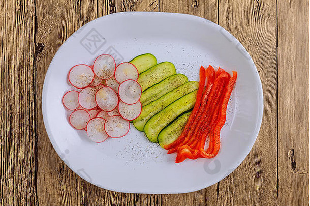 新鲜的切片蔬菜放在木制背景上的盘子上。用香料调味的蔬菜：盐、黑胡椒粉和红胡椒粉，以及少量胡椒粉