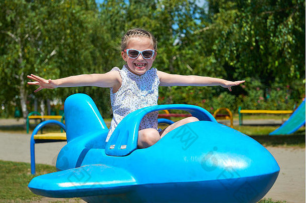 小女孩在城市公园的蓝色飞机上飞行，快乐童年，暑假概念