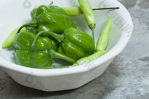 绿色哈巴内罗辣椒和塔巴斯科辣椒装在一个白色碗里，在一个粗糙的铝表面上