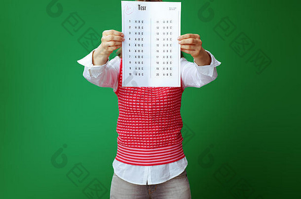 穿着灰色牛仔裤和粉色无袖衬衫的现代学生，在绿色背景下，正面举着 的考试成绩。