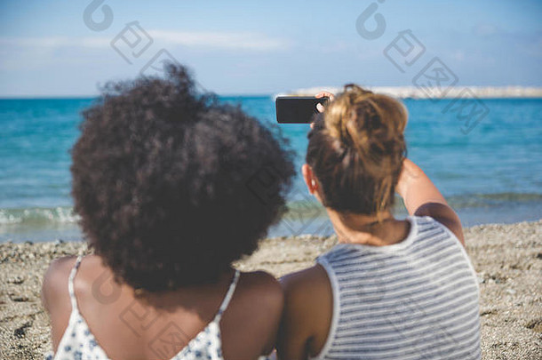 海滩上两名女子通过手机自拍的背面照片