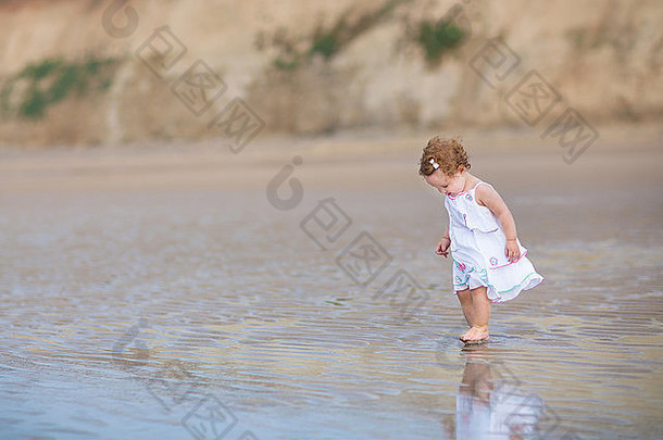 美丽的<strong>小</strong>，<strong>卷发</strong>，穿着白色连衣裙，日落时在海滩上散步