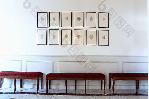 现代白色大厅中红色天鹅绒坐凳上方的镶框图片集，带护墙板
