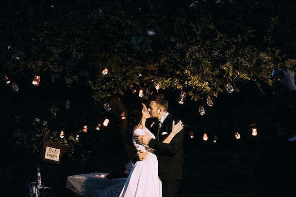 美丽的新娘新郎接吻晚上公园树装饰灯笼