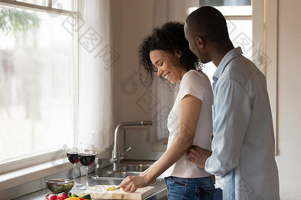 快乐的男人拥抱快乐的黑人女人准备食物。