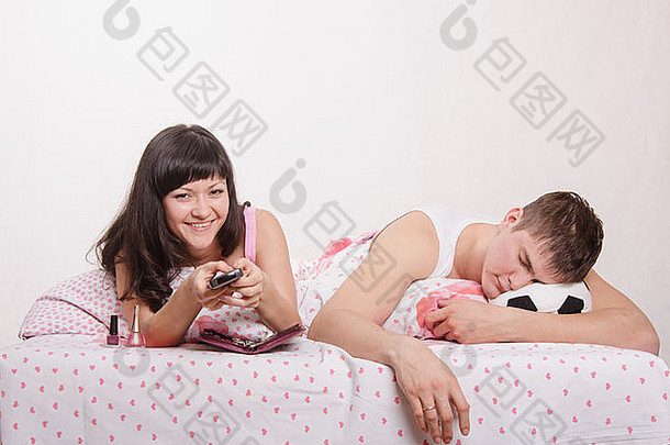 一个年轻的女孩和一个躺在床上的男人。那个漂亮的女孩手上修了指甲，那个在电视上看足球的家伙