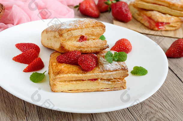 木制背景盘上的甜甜可口的泡芙糕点甜点。美味的饼干，草莓酱，浆果和糖粉