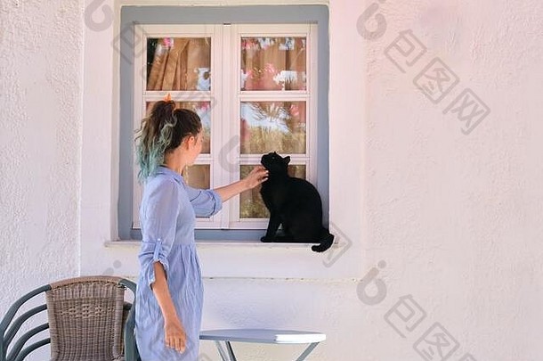 少女抚摸着坐在室外窗台上美丽的黑猫