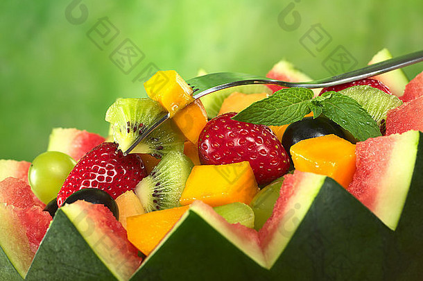 瓜钵中的新鲜水果沙拉（草莓、猕猴桃、芒果、葡萄），叉子上有猕猴桃和芒果，装饰物为薄荷叶