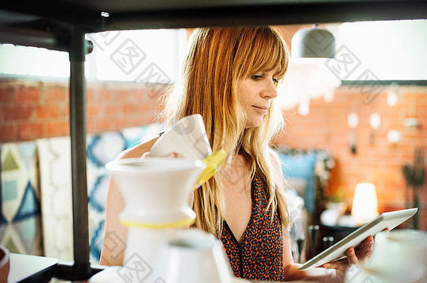 一名妇女在商店里拿着一个数字平板电脑和一个小陶瓷壶