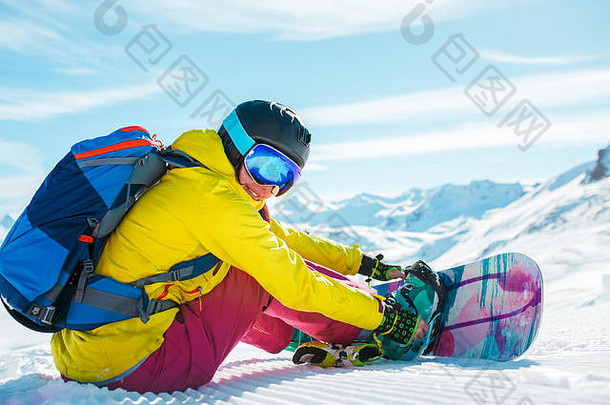 戴着头盔、背着背包、坐在雪地上玩滑雪板的女人的照片