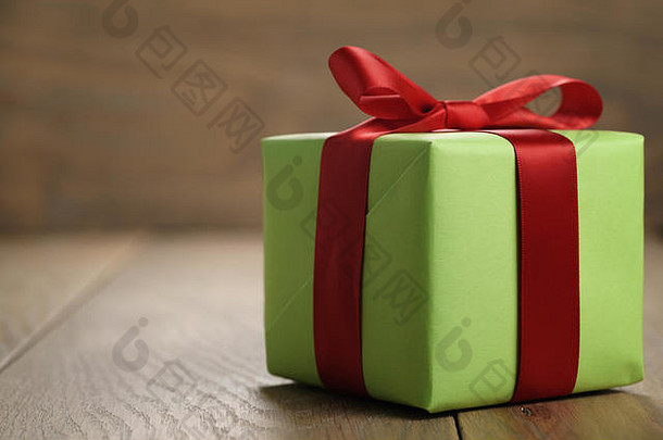 橡木桌上带有<strong>红色</strong>丝带蝴蝶结的简单绿纸礼品盒，带有复印空间