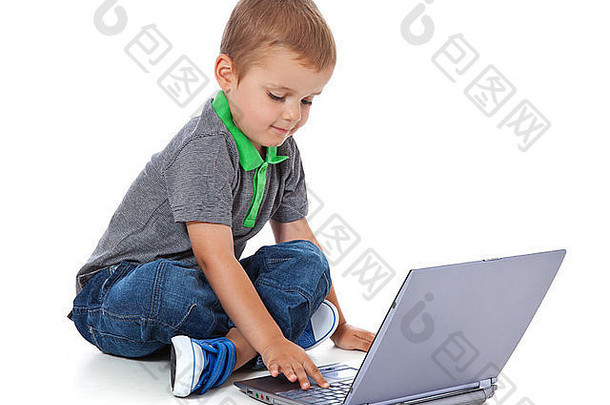 一个可爱的小男孩坐在地上拿着电脑的全长照片。全部隔离在白色背景上。