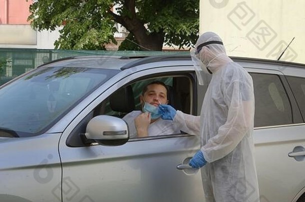 身穿危险品防护服的医务人员从鼻子向坐在汽车座椅上的男子采集拭子样本