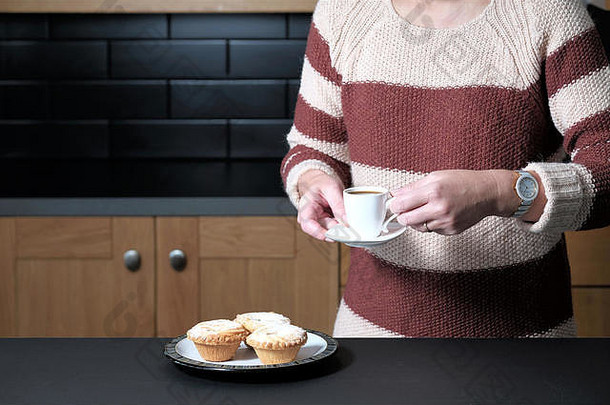 一位衣着潇洒的女士端着一杯浓咖啡，站在家里的厨房里端着一盘肉馅饼
