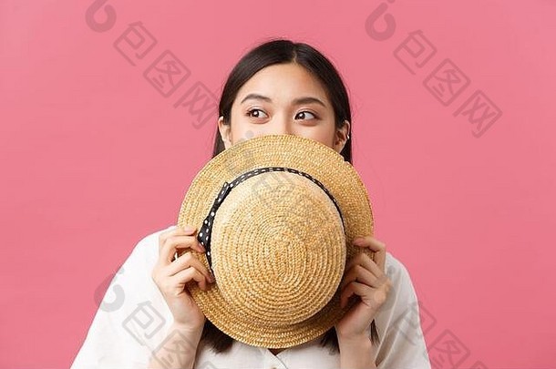美、人的情感与夏季休闲理念。梦幻般美丽的亚洲女孩把脸藏在草帽后面，偷看宣传片的特写镜头