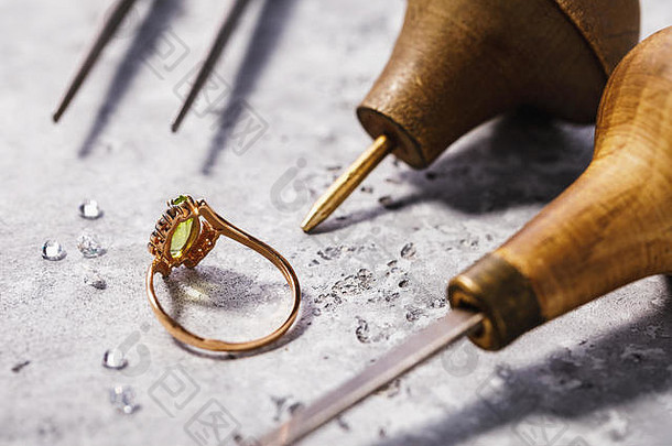 桌上镶有宝石的金戒指，周围有珠宝修复工具