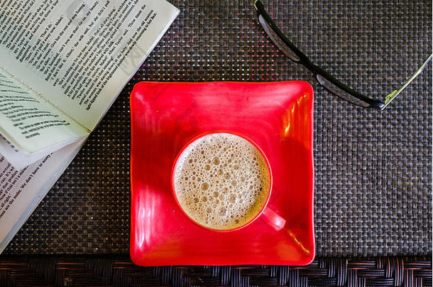 正上方是<strong>一</strong>个红色咖啡杯，旁边放着<strong>一</strong>本打开的书和<strong>一</strong>副眼镜。