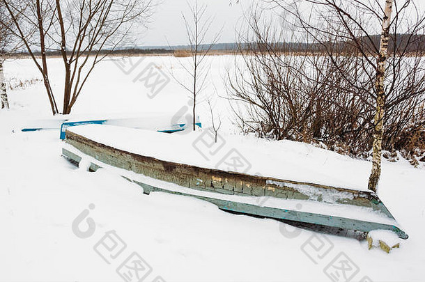一艘废弃在河岸上的旧渔船。冬季景观
