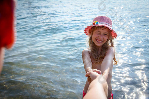 要求跟我来。戴着夏天帽子的快乐小女孩手牵着手，邀请他们的父母和她<strong>一起</strong>去海水里。