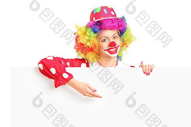 一个脸上带着快乐表情的女小丑在白色背景上的白色面板后面摆姿势