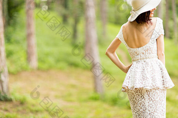 在夏季公园里，一位身穿白色连衣裙、戴着帽子的年轻女子摆姿势