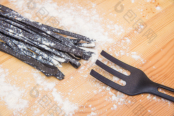 静物画：黑色意大利面、面粉、木桌上的叉子