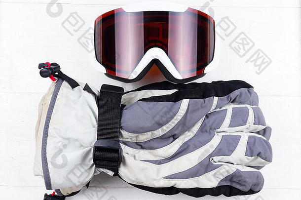 白色天然木质桌子背景上的冬季手套和护目镜。滑雪或滑雪板的概念。平放俯视图。