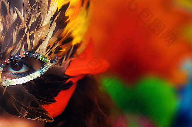 年轻女子戴着五颜六色的羽毛嘉年华面具，背景色彩鲜艳，目光接触，化妆师