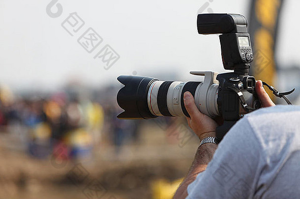 摄影师手持DSRL相机的手的细节，相机上连接有长变焦高端镜头。