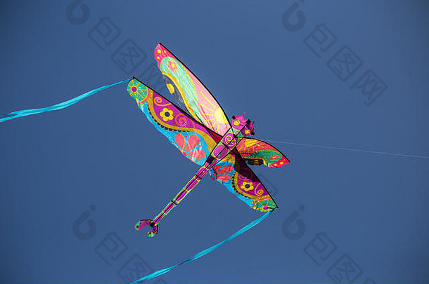 五颜六色的蜻蜓风筝，有着蓝色的尾巴和一根绳子，在蓝色的天空中飞翔，曝光更暗