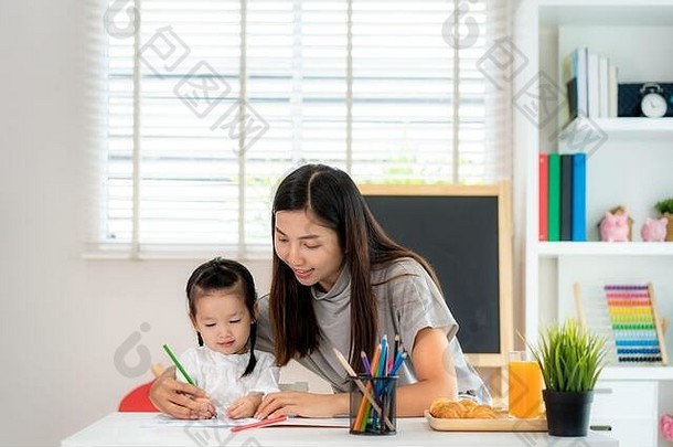亚洲幼儿园女学生和母亲在家用彩色铅笔在书上画画，在家上学和远程学习。