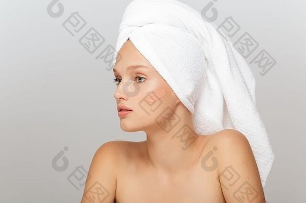 年轻漂亮女人的肖像，白色的毛巾，头上没有化妆，若有所思地用遮瑕膏抹在脸颊上