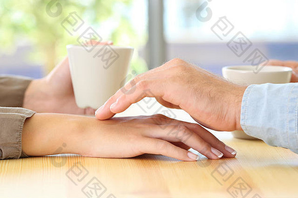 一名男子在咖啡店或家中的桌子上约会时触摸伴侣手的特写镜头