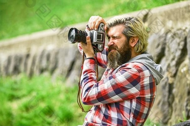 摄影师概念。摄影师业余摄影师自然背景。内容创建者。留着大胡子的时髦摄影师手持复古相机。精彩镜头。留胡子的男人在拍照。