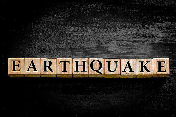 地震这个词。木制小立方体，黑色背景上有字母隔离，并留有复印空间。浪费概念形象。
